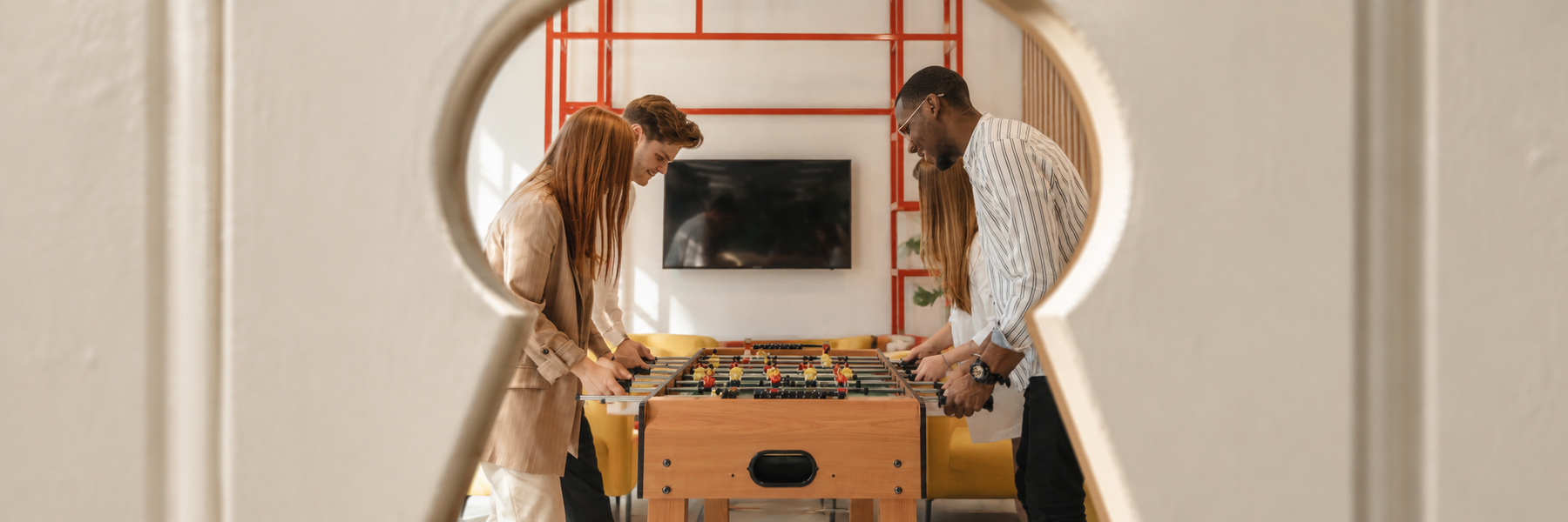 A group of friends playing on a foosball table in Airbnb peeping through a keyhole