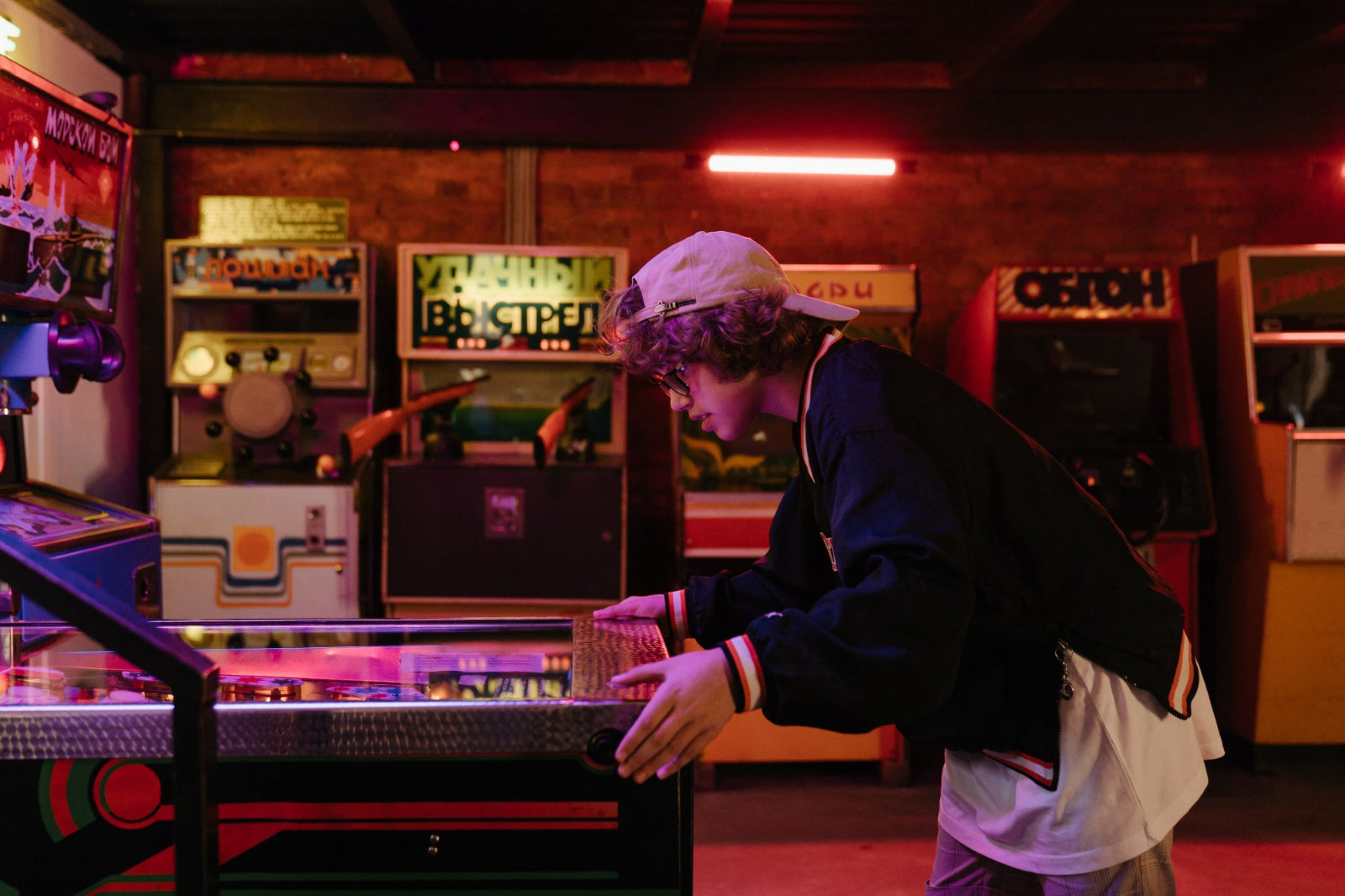 A kid leaning over a pinball machine in an arcade room