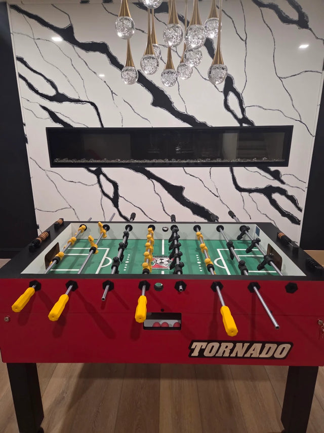 Red Tornado foosball table in a modern interior with a black-and-white marble fireplace wall