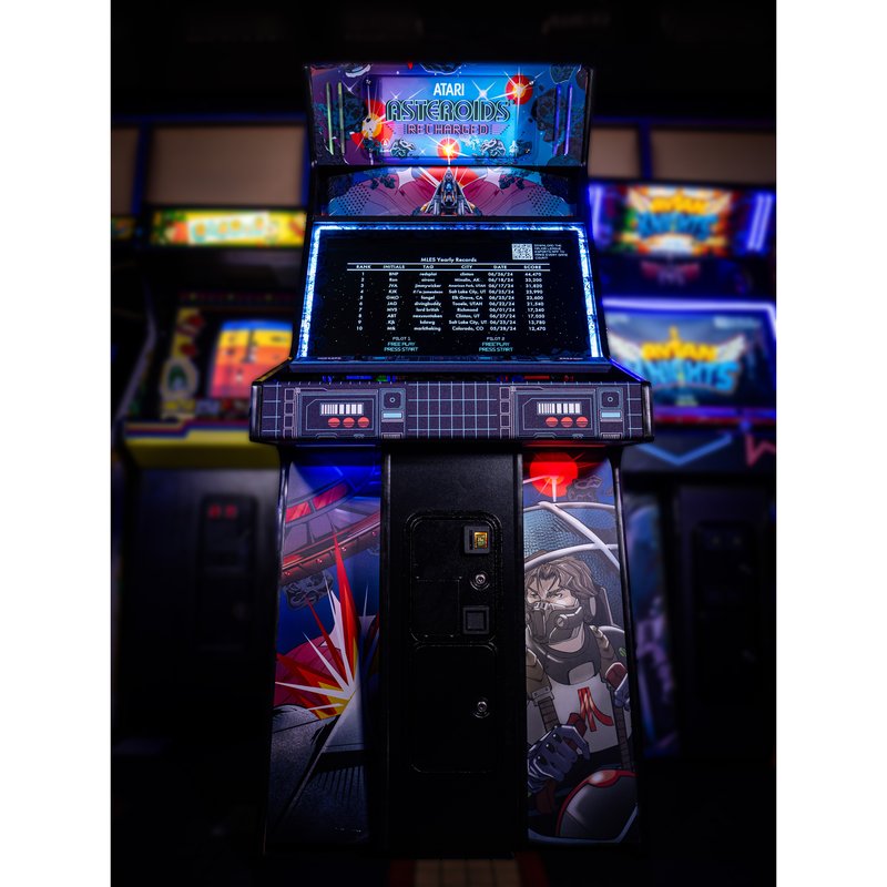 Atari Asteroids Recharged Pro+ arcade cabinet by Alan-1 on location at Flynn's Retrocade in Utah, straight on front view showing the illuminated Atari Asteroids Recharged marquee and the MLeS yearly records leaderboard on screen.