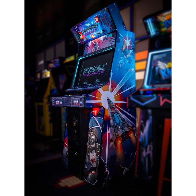 Atari Asteroids Recharged Pro+ arcade cabinet by Alan-1 installed on location at Flynn's Retrocade in Utah, front three quarter view showing the lit cyan T-molding, the spacecraft and pilot side art and the attract screen set to free play.